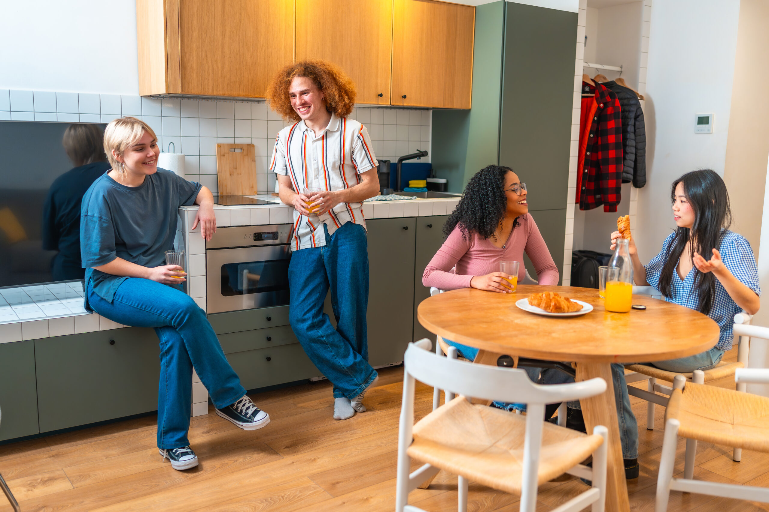Happy multi ethnic friends spending leisure time together, having breakfast and talking in a modern kitchen